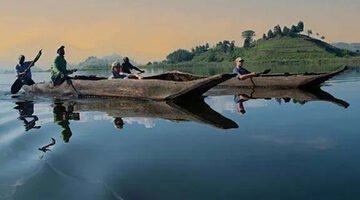 Tourists on a guided canoe safari at Lake Mutanda, spotting birds along the bank.